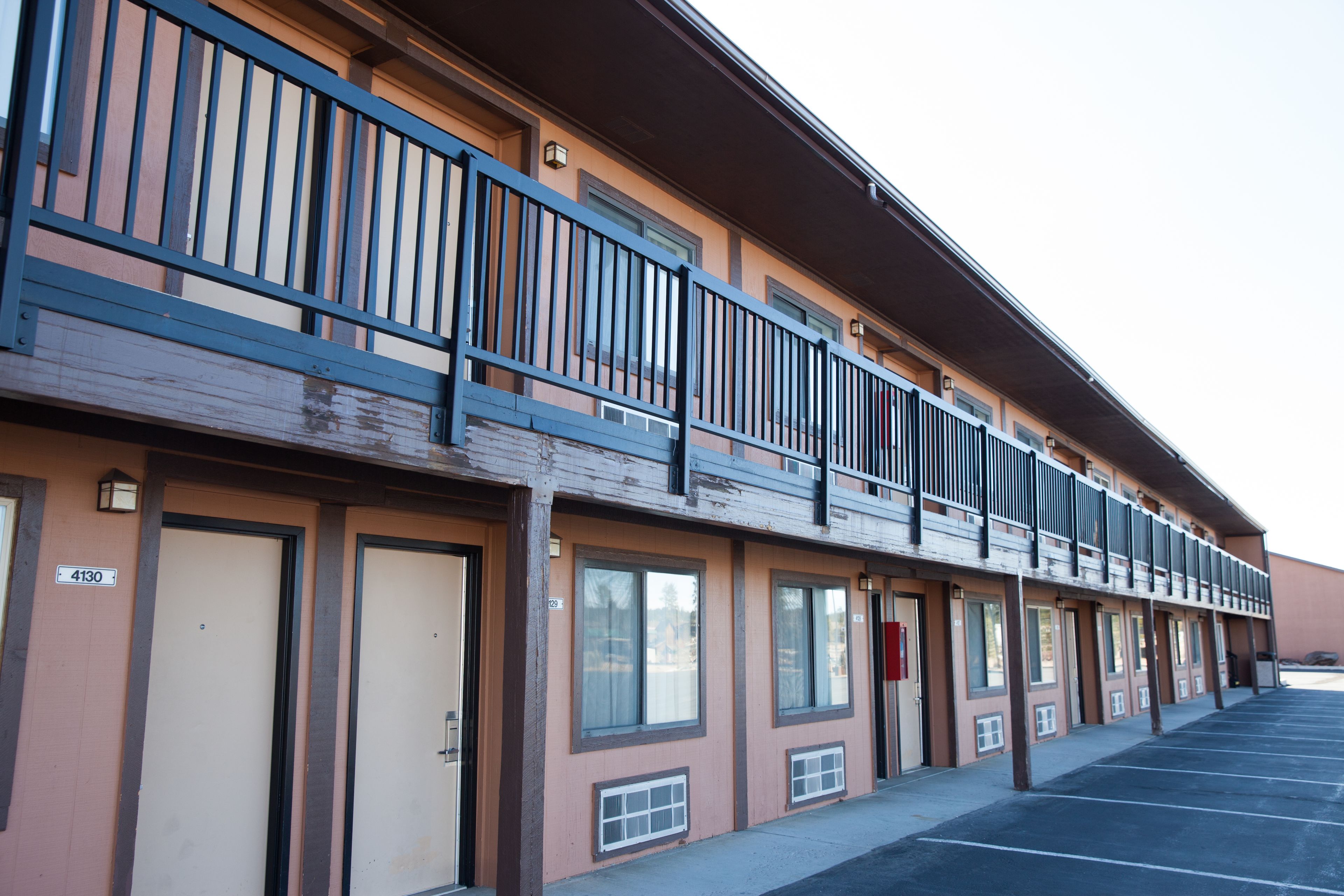 Un motel avec une rangée de chambres, chacune dotée d’une porte et d’une fenêtre. Au deuxième étage, un balcon est agrémenté d’une balustrade.