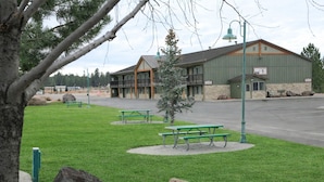 A building with a green exterior and a stone base, a parking lot, and picnic tables.