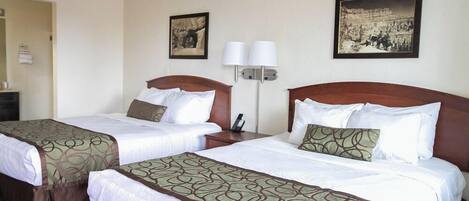 Ein Hotelzimmer mit zwei Betten, jeweils mit einem gemusterten Überwurf, einem Nachttisch mit Lampe und zwei gerahmten Bildern an der Wand.