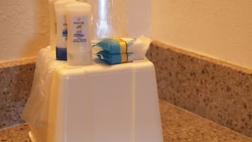 Ein Badezimmerbereich mit einer Ablage, auf der Toilettenartikel liegen, darunter eine Pantene-Shampoo-Flasche, eine Lotionflasche und eine Plastiktüte.