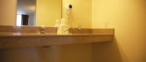 Un baño con encimera de granito, un secador de pelo y un espejo.