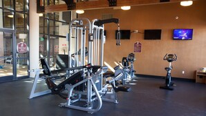 A gym with various exercise machines, a television on the wall, and large windows.