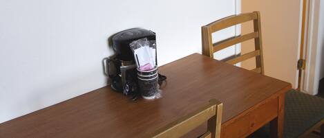 Mesa de jantar de madeira com uma cafeteira e duas cadeiras.