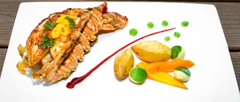 A white plate with a grilled fish, lemon slices, and a red sauce.