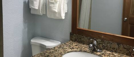 A bathroom with a granite countertop sink, a white toilet, and two white towels hanging on a towel rack.