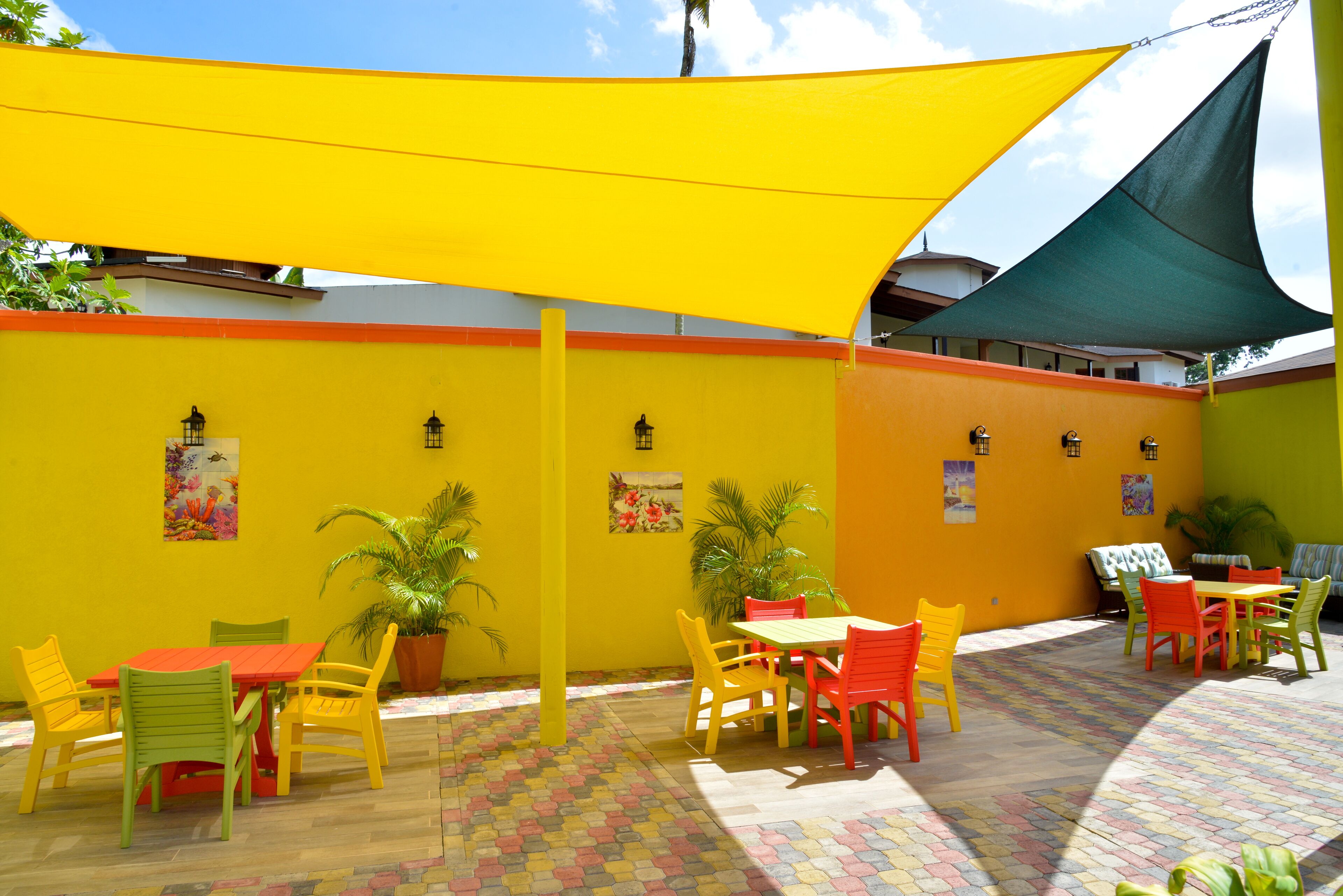 An outdoor patio area with yellow and orange walls, a tiled floor, and colorful chairs and tables.
