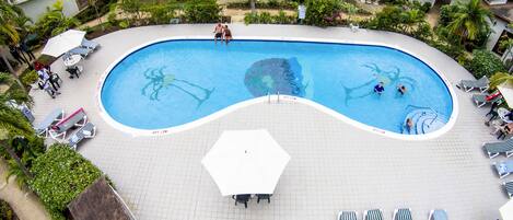 An aerial view of a hotel with a large swimming pool surrounded by lounge chairs and a garden.