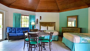 Una habitación con techo de madera, un sofá azul, una mesa de comedor con sillas, una cama con colcha verde y un aparador de madera.
