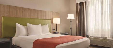 Una habitación de hotel con una cama grande, una mesita de noche, una lámpara y una ventana con cortinas.
