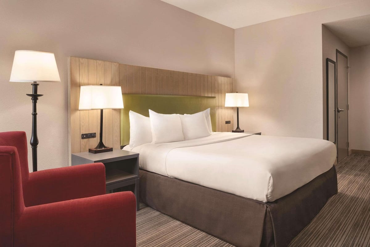 A hotel room with a large bed, two bedside tables with lamps, a red chair, and a wooden headboard.