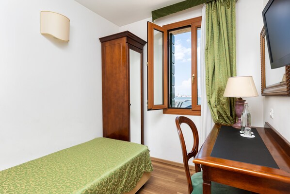 Une pièce comprenant un lit, un bureau avec une lampe, une chaise, une fenêtre avec des rideaux et un téléviseur.