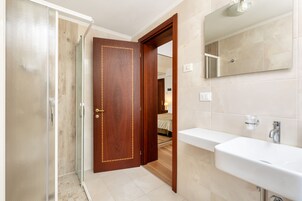 Un bagno con porta in legno, box doccia in vetro e lavandino bianco.