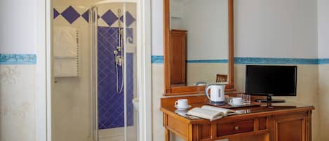 A bathroom with a shower, a vanity with a mirror, a television, and a small seating area.