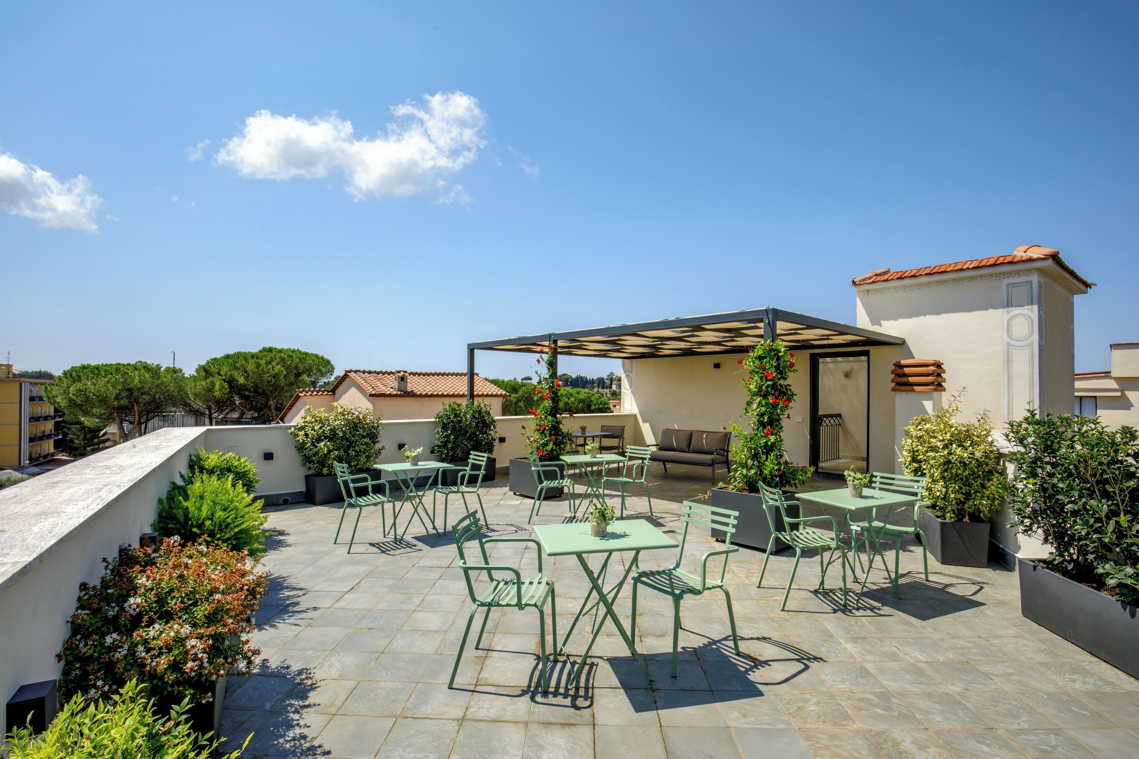 An outdoor patio with green metal furniture, potted plants, and a pergola.