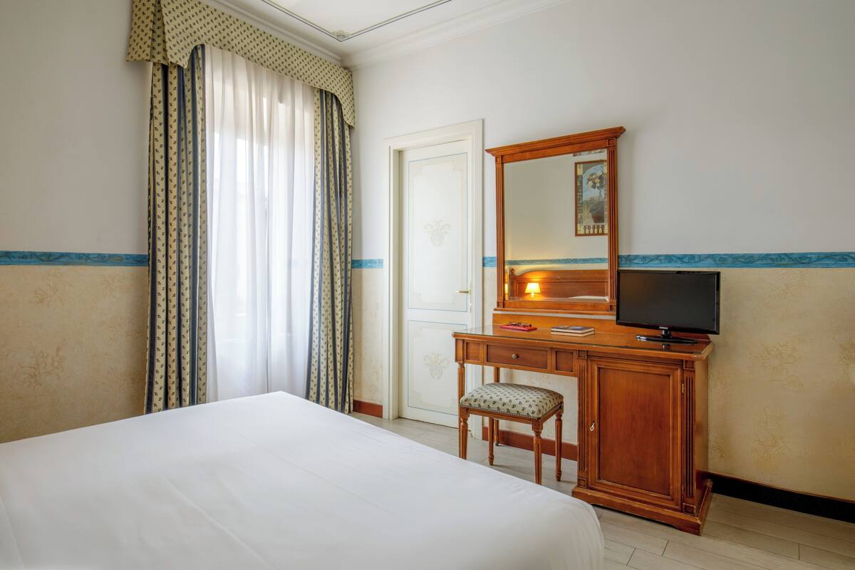 Habitación de hotel con una cama, un escritorio de madera con televisor y una silla.