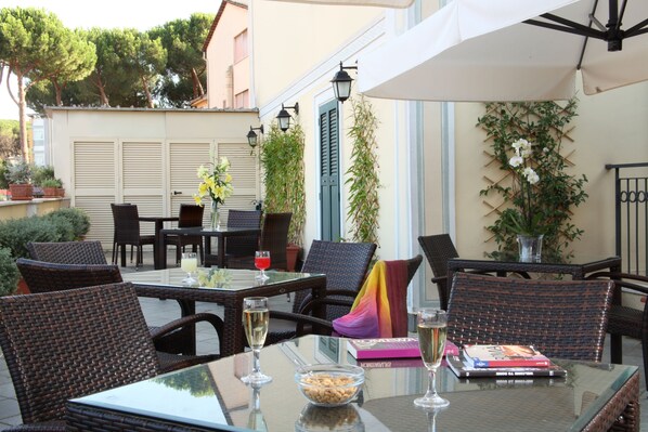 An outdoor patio with wicker furniture, a glass table, and a book. - Hotel Alessandrino (Rome)