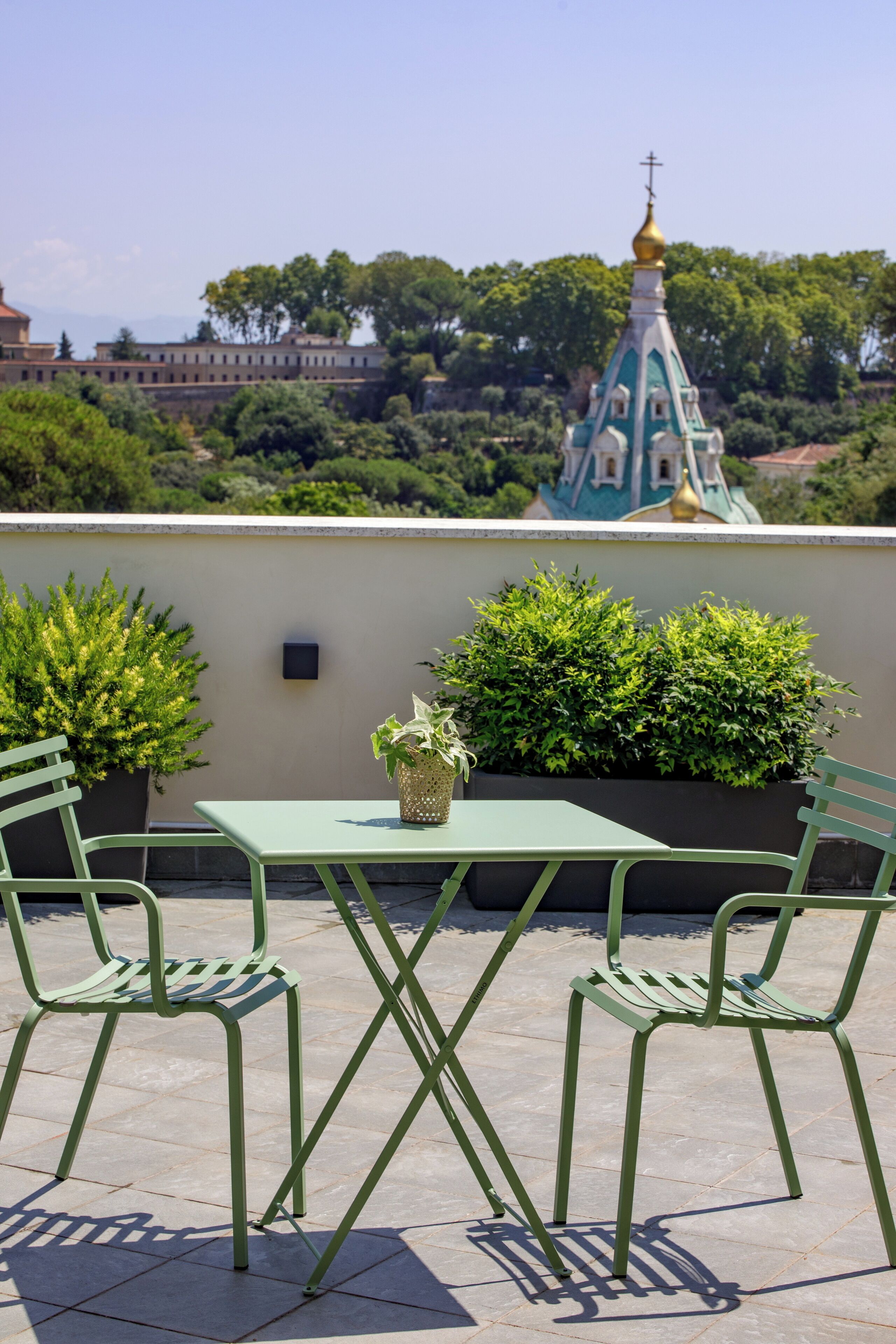 Terraza en la azotea con una mesa, sillas, plantas en macetas y vistas a una iglesia con cúpula dorada.