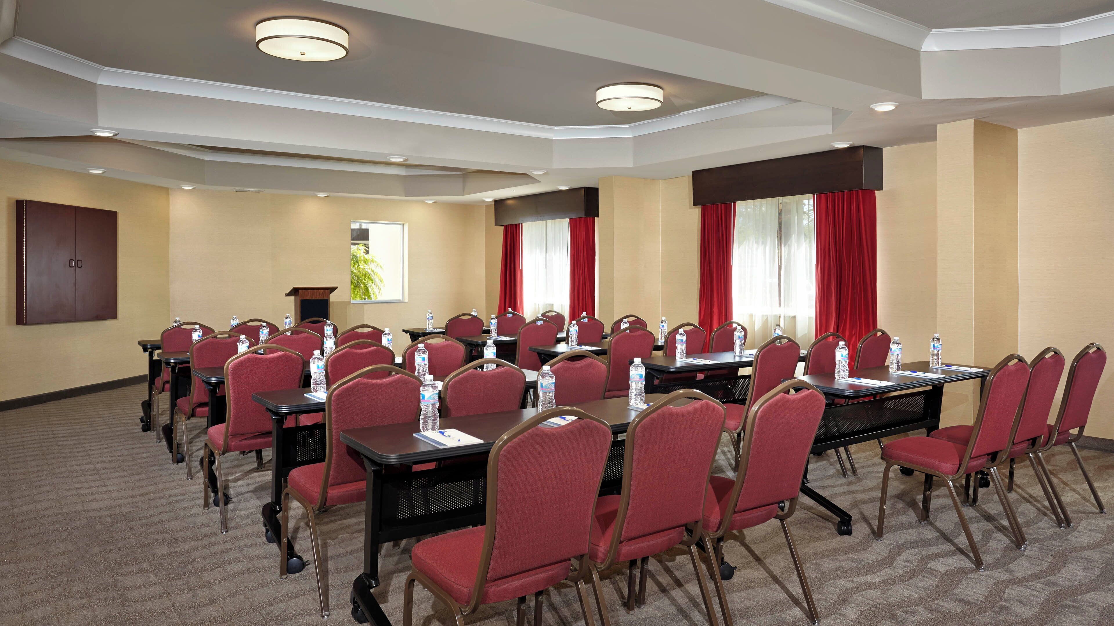 Una sala de conferències amb diverses taules i cadires, equipada amb ampolles d'aigua, en un entorn d'hotel.
