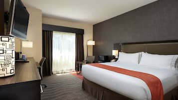 A hotel room with a large bed, a desk with a computer, a television, and a window with curtains.