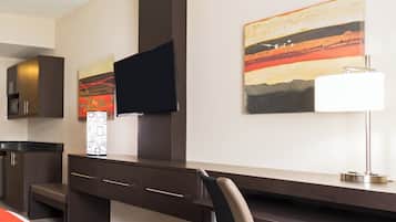Habitación de hotel con escritorio, televisor montado en la pared, un cuadro y una lámpara.