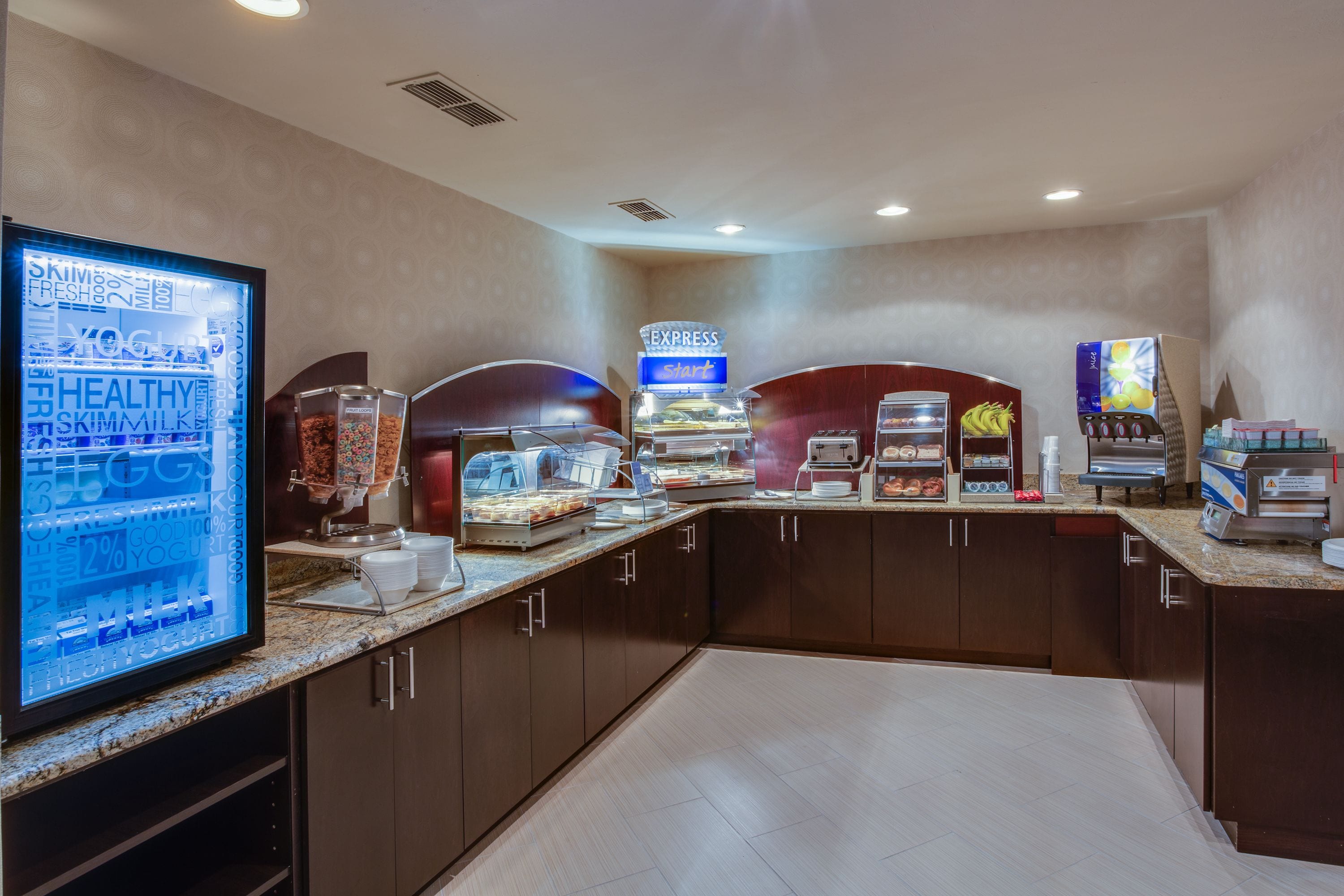 Un’area colazione con una bacheca digitale, postazioni self-service per il cibo e una macchina per il caffè.