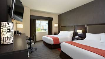 A hotel room with two beds, a desk with a TV, a lamp, and a view of the outside.