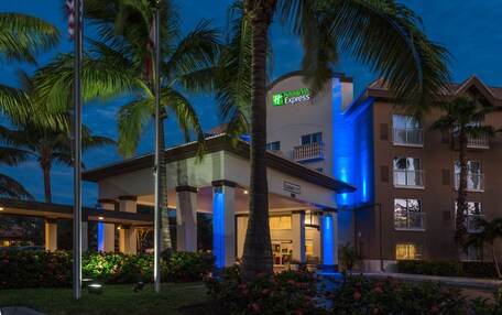 A Holiday Inn Express hotel with a modern design, featuring a prominent entrance, palm trees, and a well-lit facade.