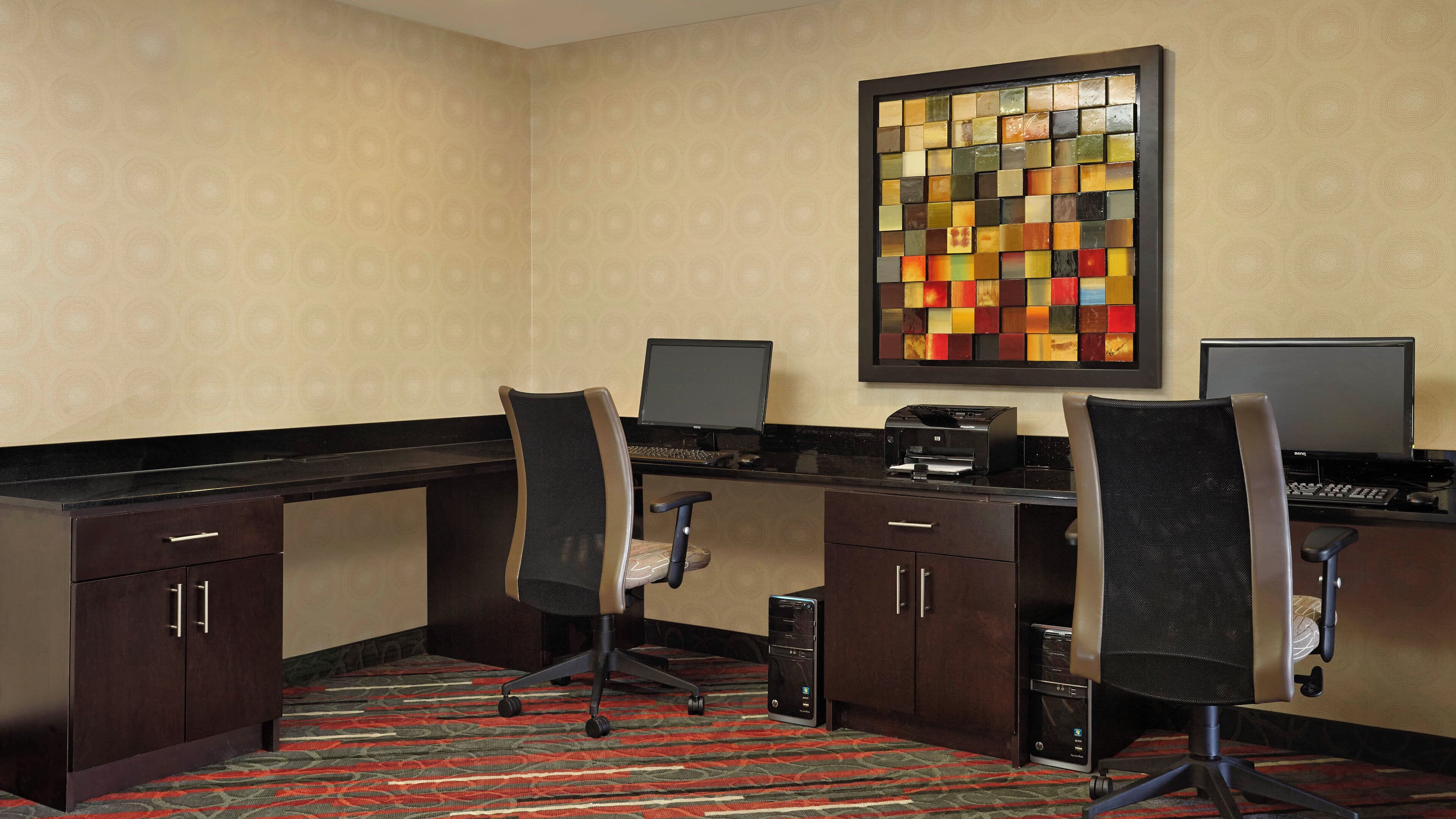 A hotel office with two desks, chairs, a printer, and a decorative wall piece.