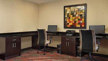 A hotel office with two desks, chairs, a printer, and a decorative wall piece.