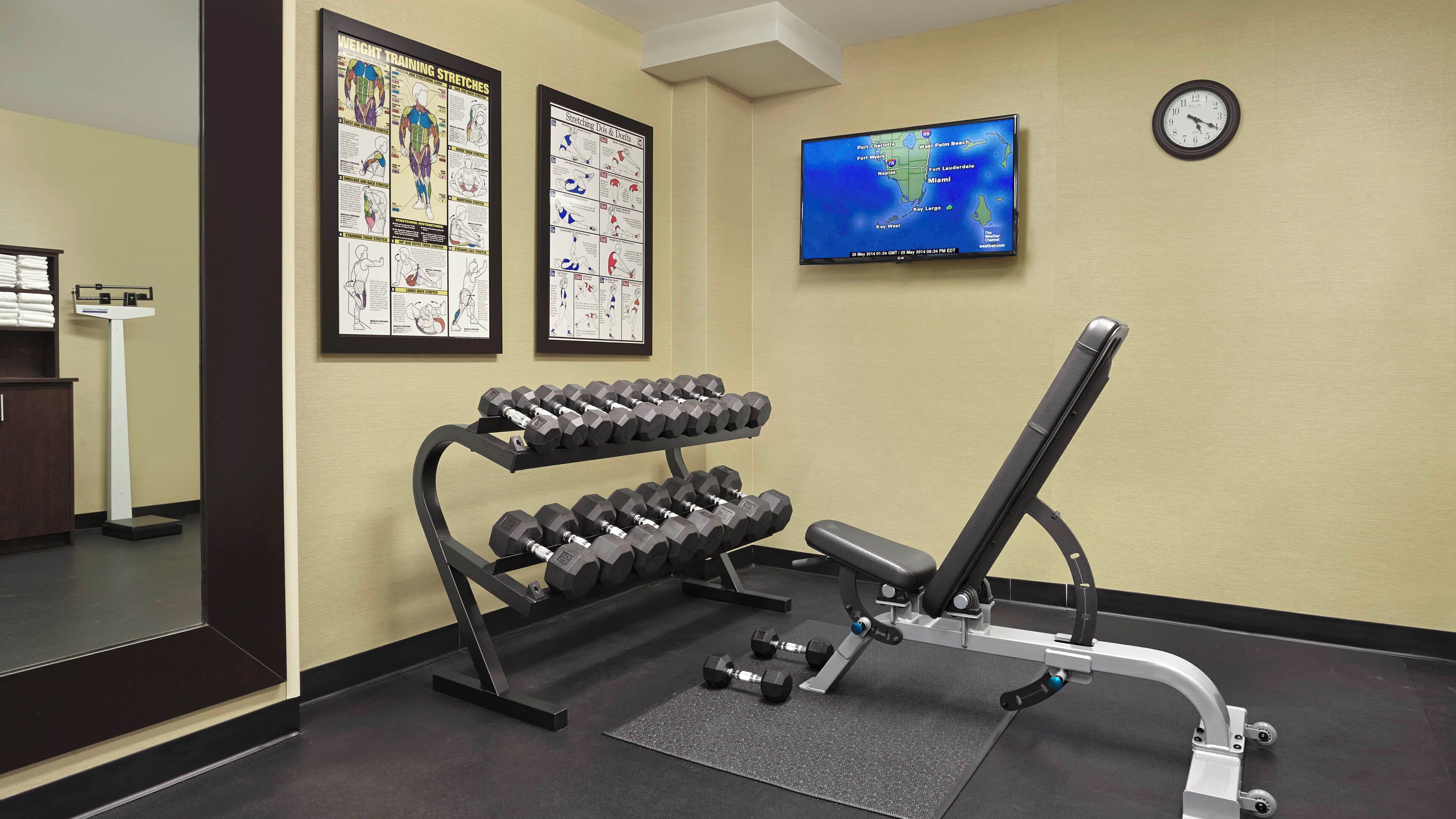 Une salle de sport équipée d’haltères, d’un banc de développé couché et de panneaux explicatifs.