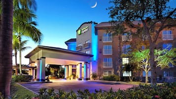 Edificio Holiday Inn Express con entrada cubierta, palmeras y una luna creciente en el cielo.
