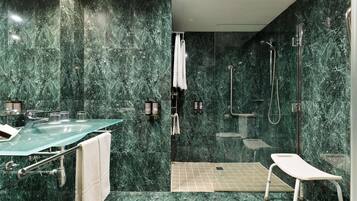 Un baño moderno con un lavabo de cristal, paredes de mármol, una zona de ducha y un perchero blanco.