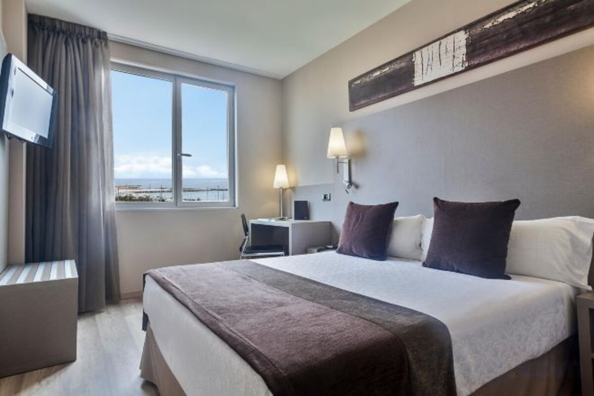 A hotel room with a bed, a desk, a chair, a TV, and a window with a view.