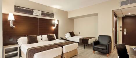 A hotel room with two beds, a desk, a chair, and a lamp.