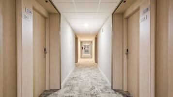 Un pasillo de hotel con puertas numeradas, una alfombra estampada e iluminación empotrada en el techo.