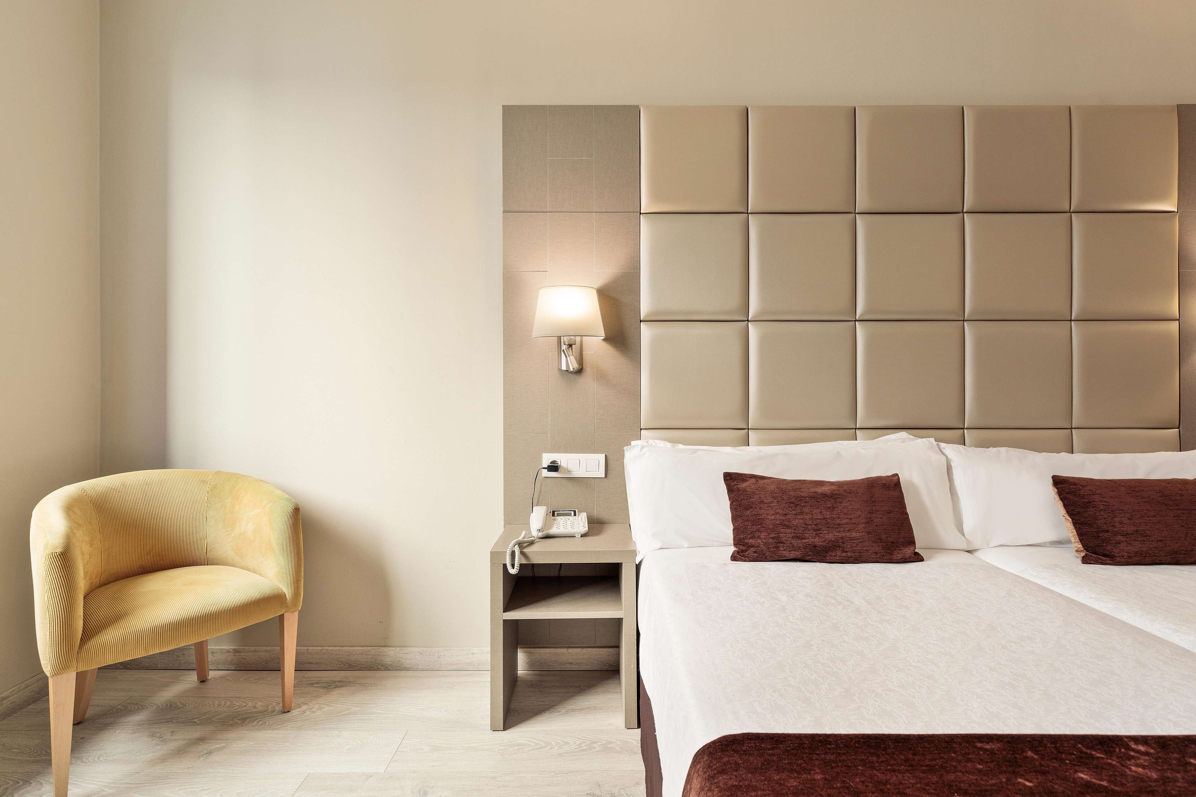 Et hotelværelse med en seng, et natbord, en lampe og en stol.