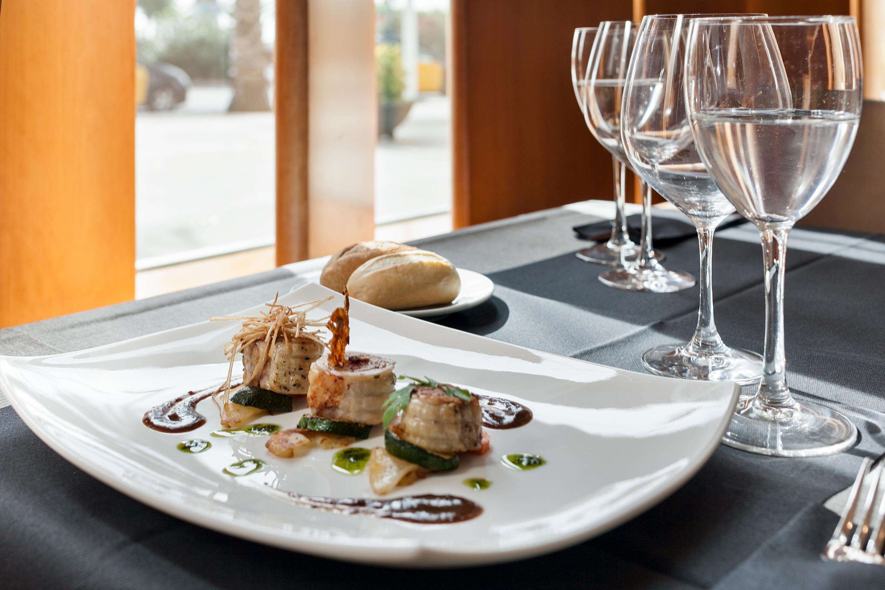 Una mesa de comedor con un plato de comida blanca, dos copas de vino y vistas al exterior.
