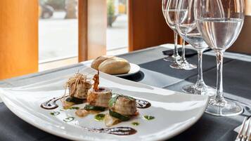 Una mesa de comedor con un plato de comida blanca, dos copas de vino y vistas al exterior.