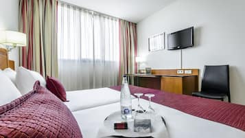 Una habitación de hotel con cama, escritorio, televisor y ventana con cortinas.