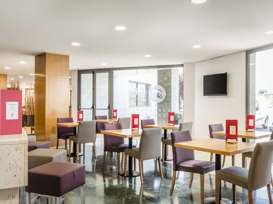 A modern hotel lobby with a reception desk, seating area, and large windows.