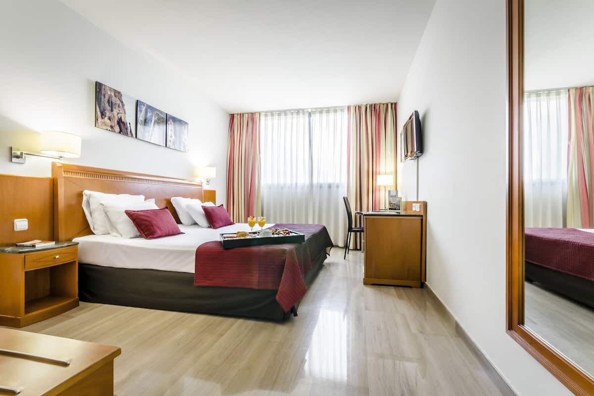 A hotel room with a large bed, bedside tables, a desk, and a TV.