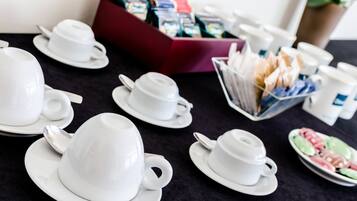 Una mesa con tazas y platillos blancos, una caja de bolsitas de té y un plato de fruta.