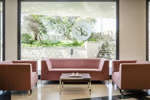 Un interior moderno con un sofá rosa, una mesita de centro y un amplio ventanal con vistas a un jardín y una escalera.