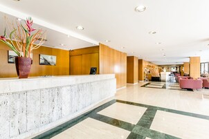 Un vestíbulo de hotel con una recepción, una planta en maceta grande y un área de descanso con sillas.