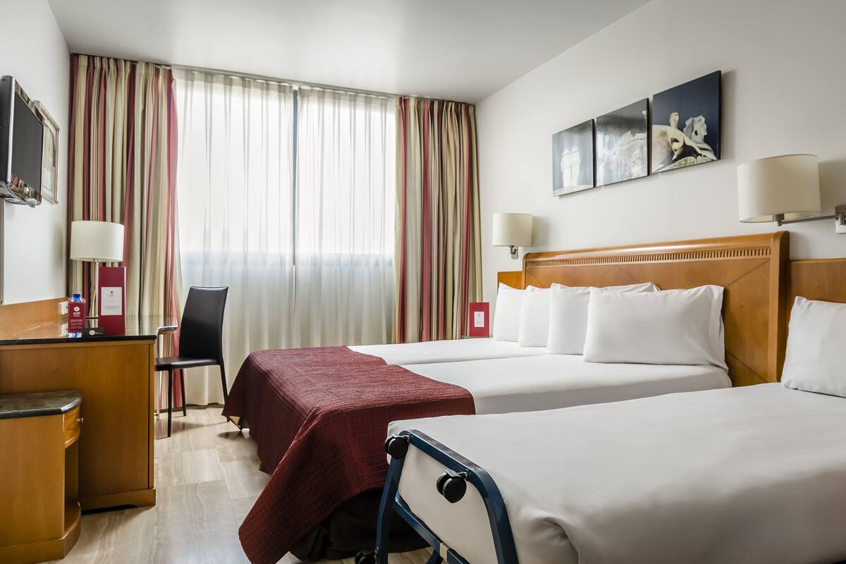 A hotel room with two beds, a desk, a chair, and a TV.