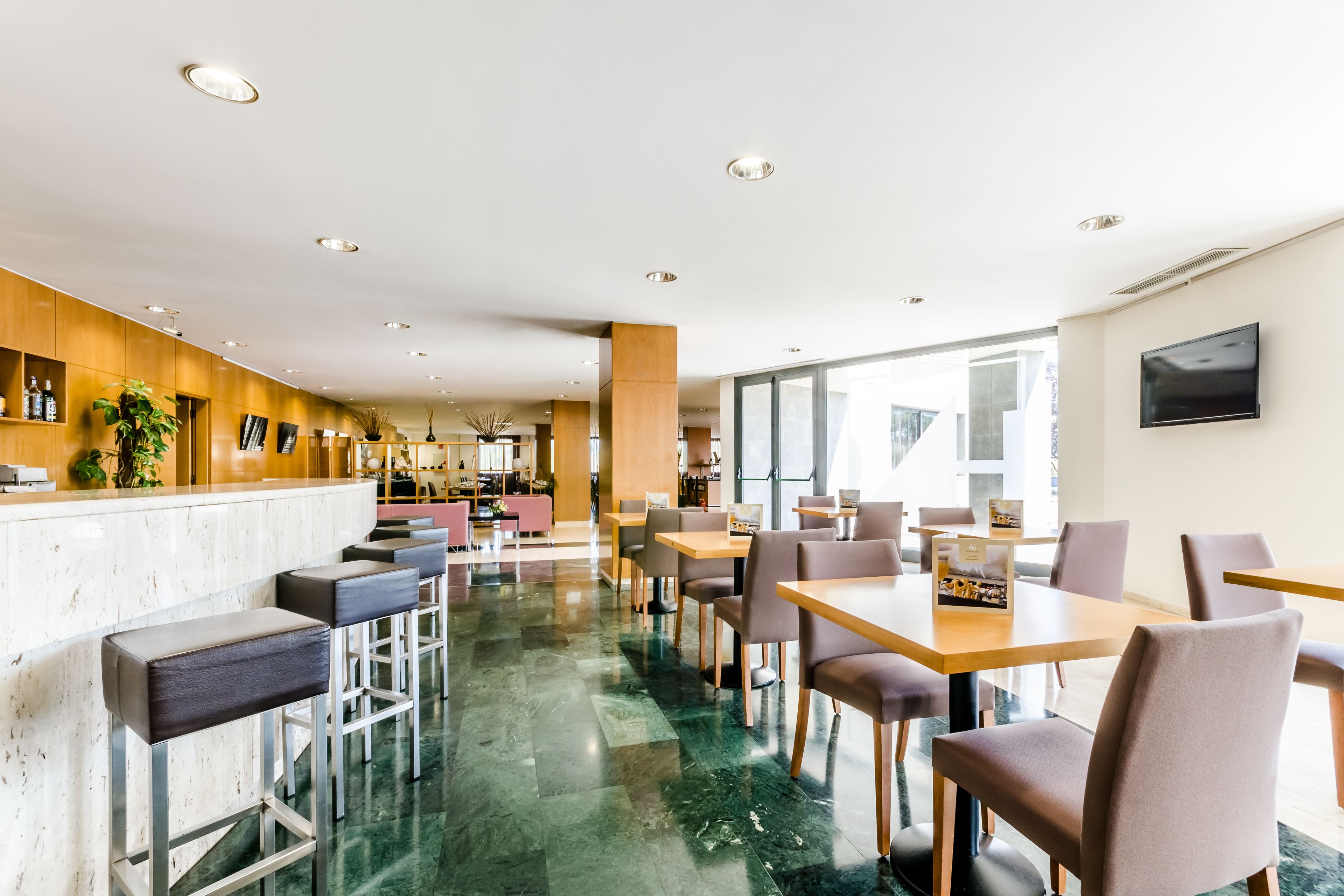 Un hall d’hôtel moderne avec un sol en marbre, un comptoir d’accueil en bois, un bar et des espaces aménagés pour s’asseoir.