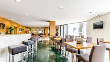 Un hall d’hôtel moderne avec un sol en marbre, un comptoir d’accueil en bois, un bar et des espaces aménagés pour s’asseoir.