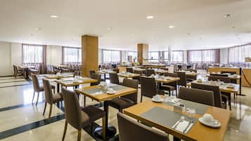 Een ruime hotel eetruimte met meerdere tafels en stoelen, grote ramen met gordijnen, en een schoon, modern design.