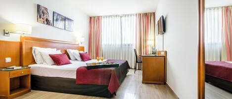A hotel room with a bed, bedside tables, a desk, a chair, and a TV.