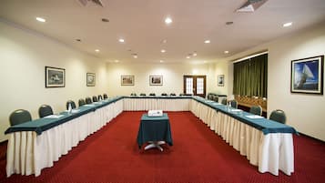 Un salón de conferencias con una larga mesa, sillas y un proyector.